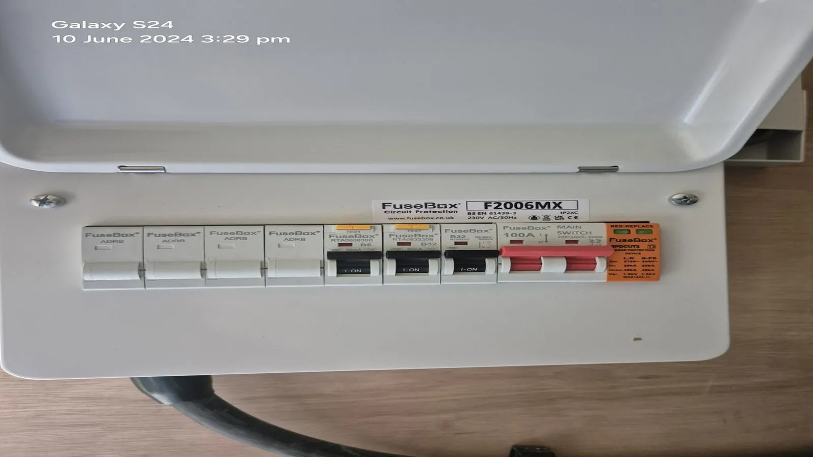 An open FuseBox consumer unit showing several labelled circuit breakers and an isolator switch, mounted on a wooden surface. The image timestamp reads Galaxy S24, 10 June 2024 15:29.