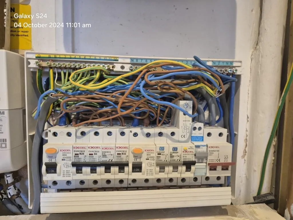An open electrical fuse box showing multiple circuit breakers and a tangle of coloured wires. The photo is timestamped 04 October 2024 11:01 am in the top left corner.