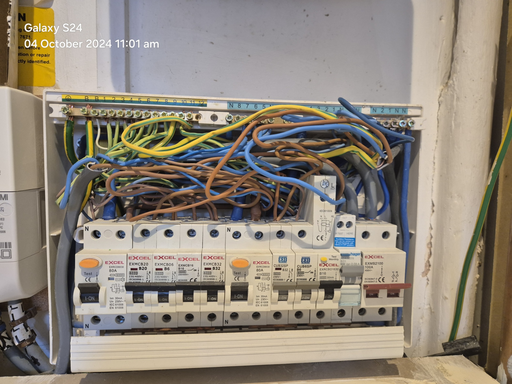 An open electrical fuse box showing multiple circuit breakers and a tangle of coloured wires. The photo is timestamped 04 October 2024 11:01 am in the top left corner.