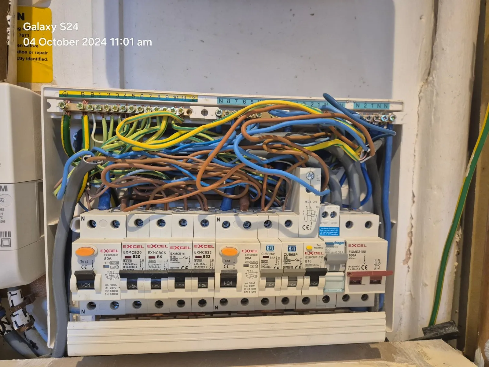 An open electrical fuse box showing multiple circuit breakers and a tangle of coloured wires. The photo is timestamped 04 October 2024 11:01 am in the top left corner.
