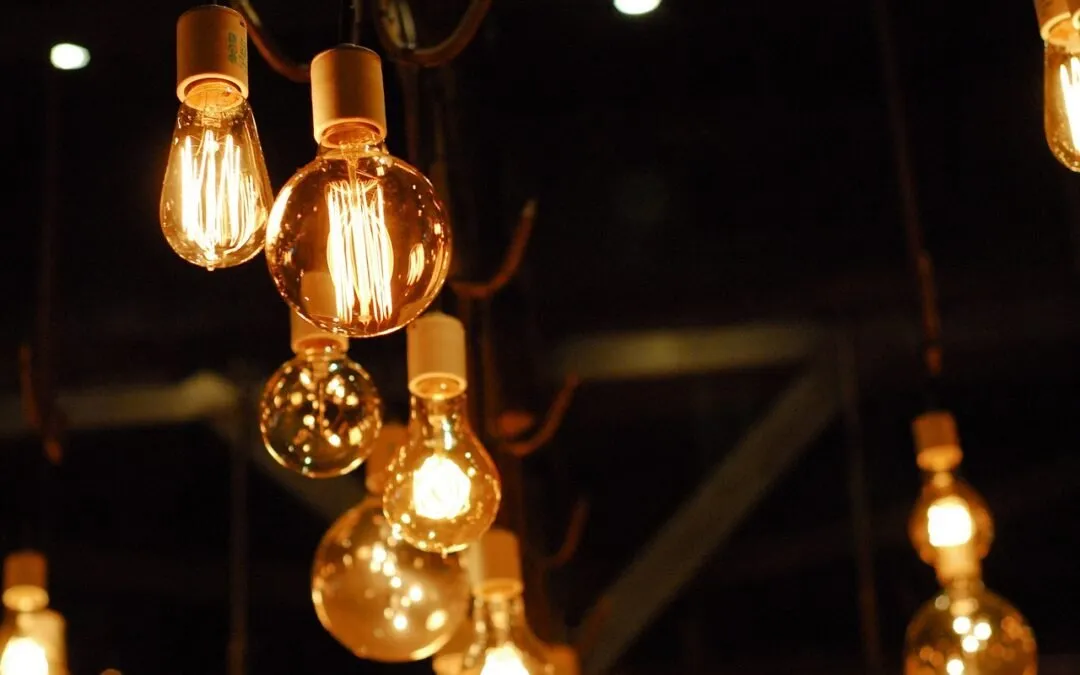 A close-up of several vintage-style incandescent light bulbs hanging from the ceiling, glowing warmly against a dark background.