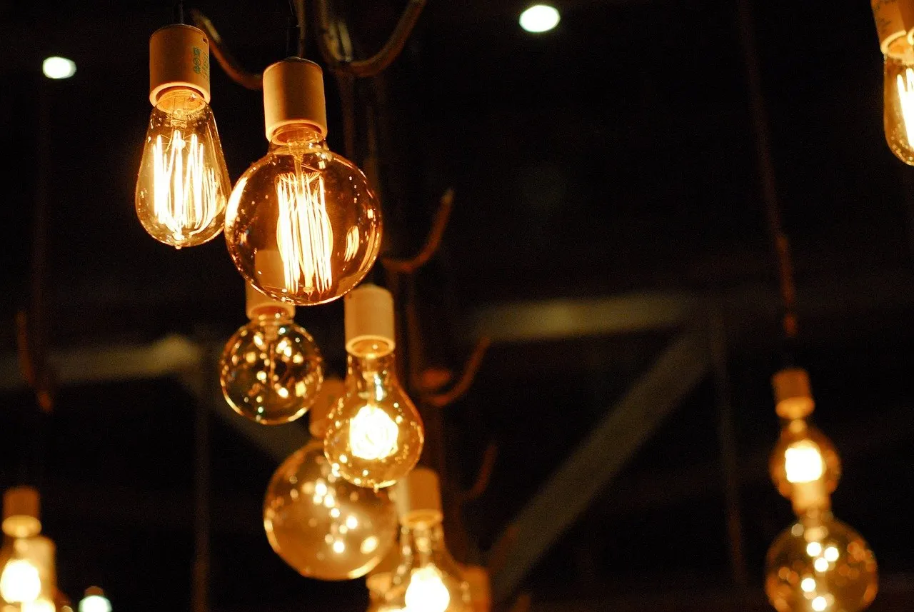 Several vintage-style Edison light bulbs hang from the ceiling, emitting a warm, soft glow against a dark, blurred background, creating a cosy and ambient atmosphere.