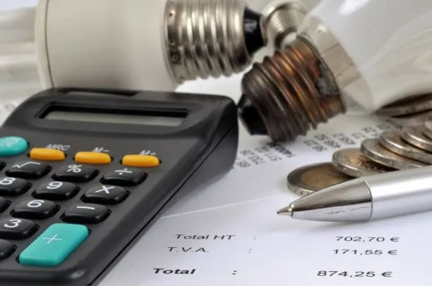 A calculator, a pen, coins, and two light bulbs rest on a utility bill, evoking energy costs and calculations—perfect for those seeking an accurate electrical service estimate or using an electrician cost calculator.
