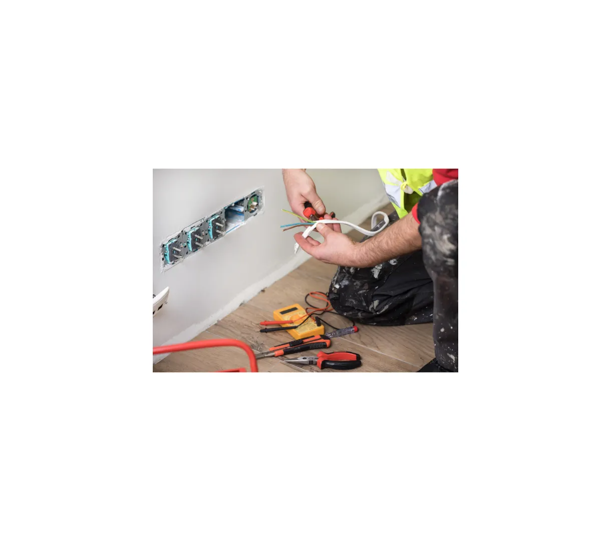 Electrician Prices SW London A person in work clothes repairs electrical wiring next to an open wall socket, with tools such as pliers, screwdrivers, and a voltage tester on the floor—just another day for Buildspark, known for fair electrician prices in SW London.