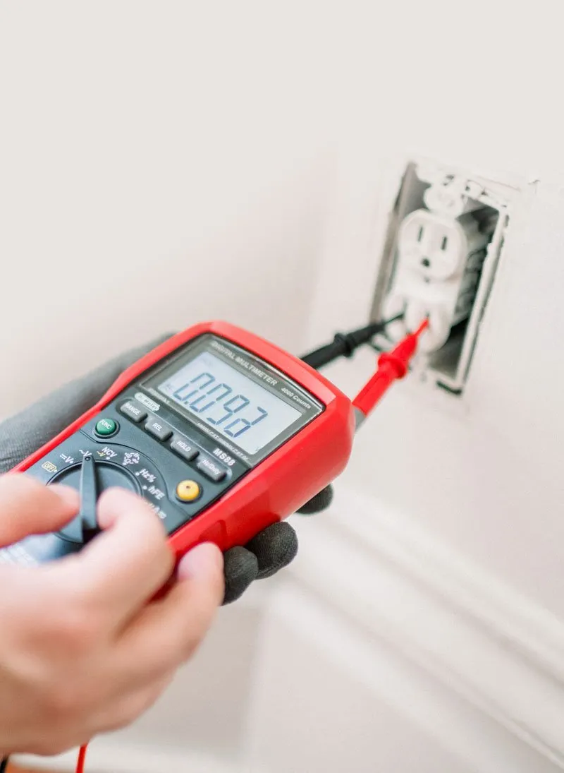 Qualified electrician in Balham testing a wall socket with a digital multimeter during an electrical safety inspection.