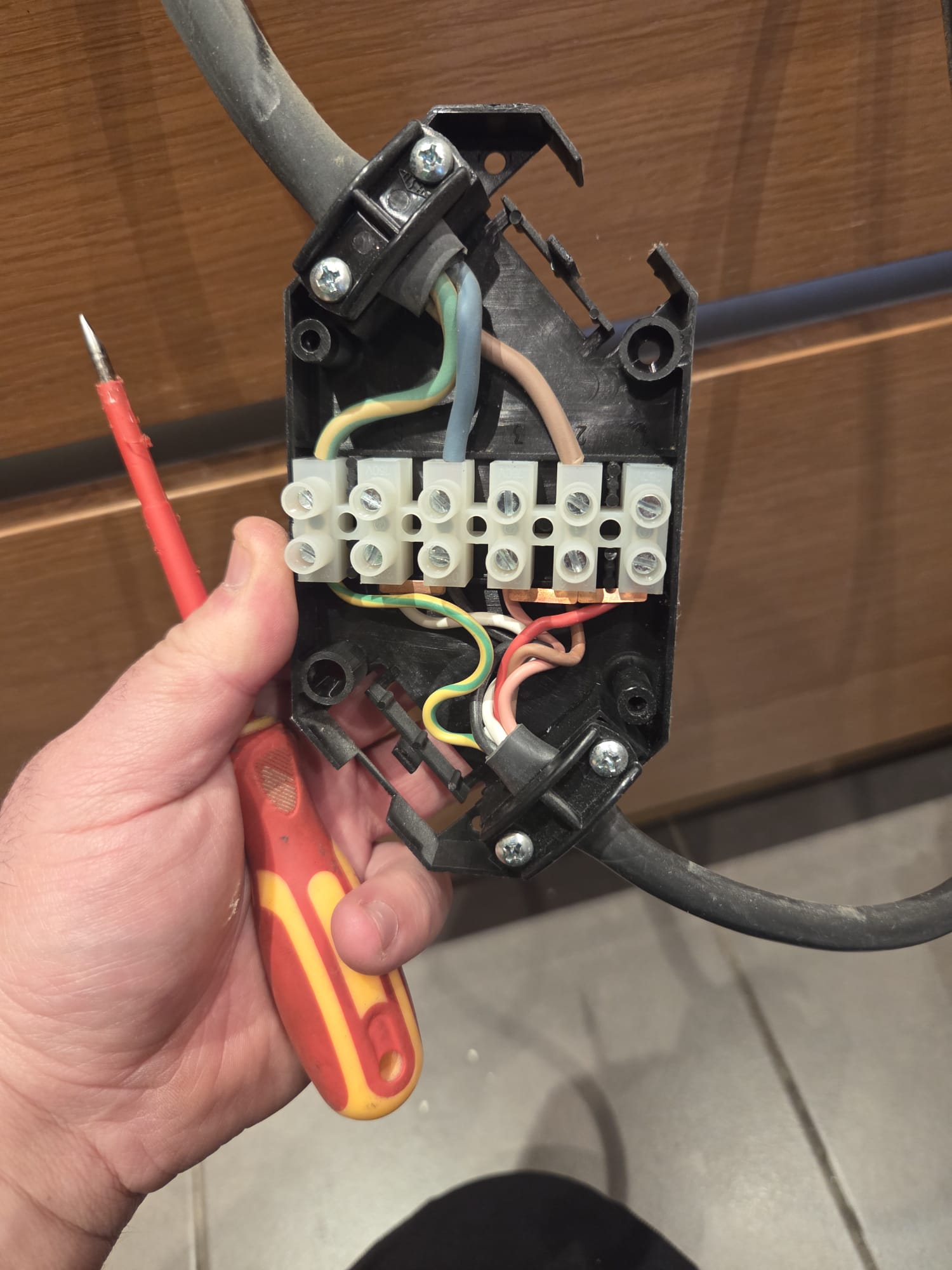 Trusted electrician repairing faulty cooker wiring with screwdriver and connector block Close-up of an electrician using a screwdriver to repair faulty block connectors inside a built-in cooker appliance.